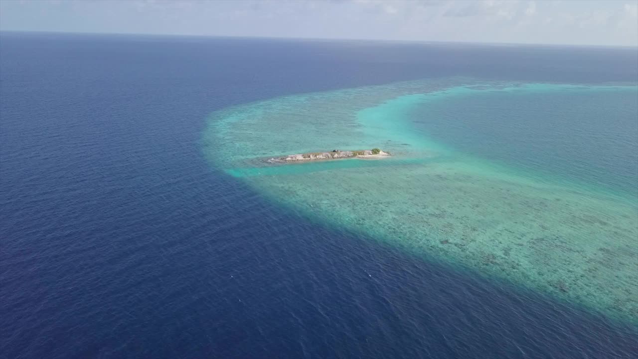 鸟瞰图的岩石形成在蓝绿色的海对天空，无人机向前飞行在阳光明媚的一天-南马累环礁，马尔代夫视频素材