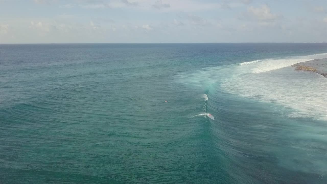 空中平拍的人冲浪在海浪上对着天空，无人机飞过溅水-南马列环礁，马尔代夫视频素材