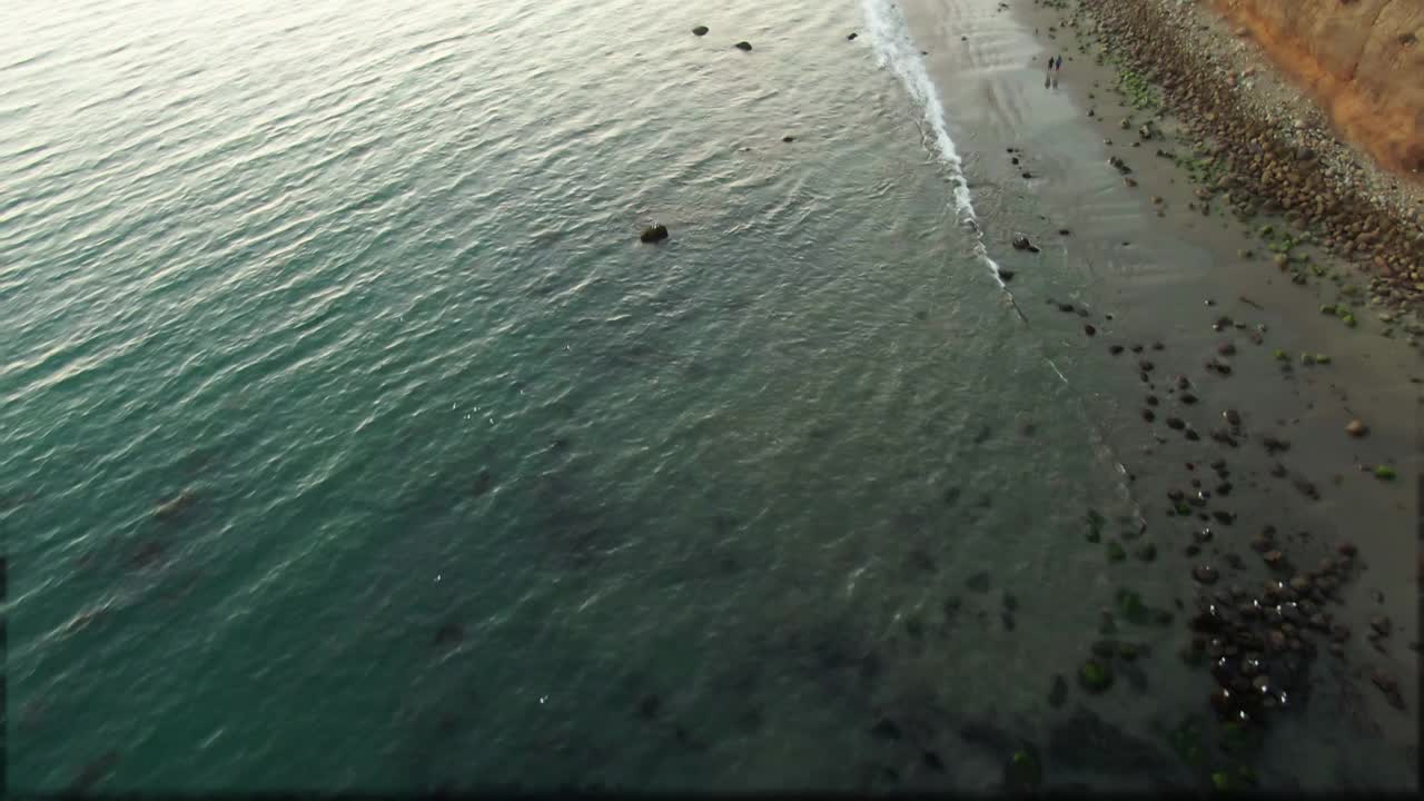 空中倾斜上拍的海浪溅在海滩上的蝴蝶，无人机下降在海上的悬崖对天空在日落-圣巴巴拉，加利福尼亚视频素材