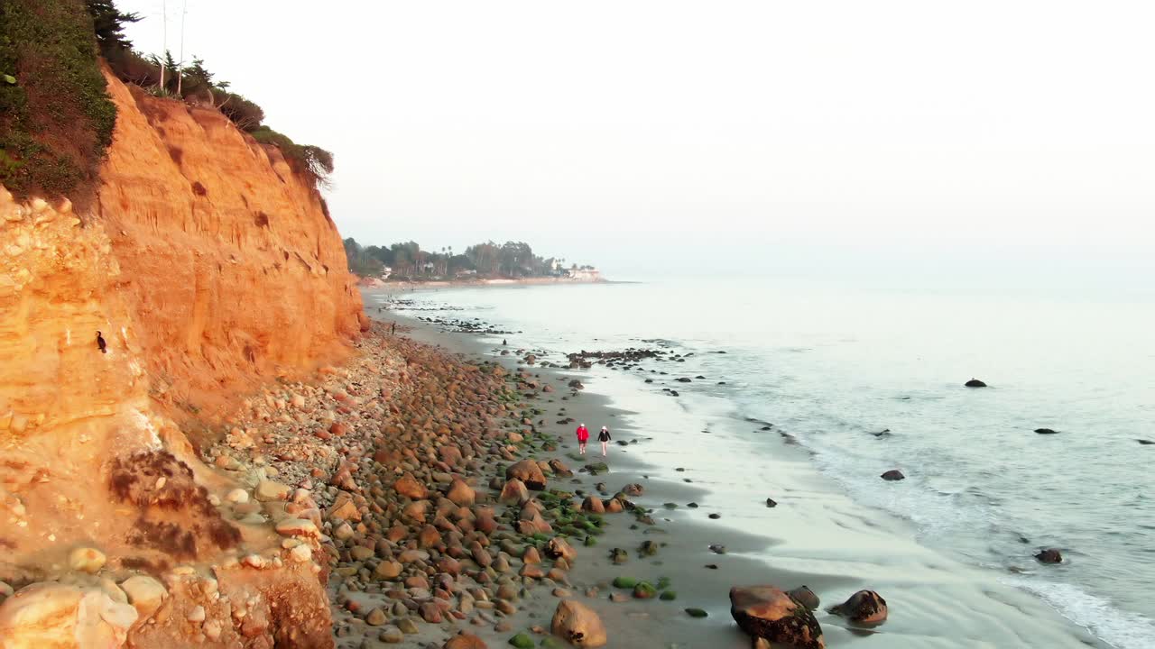 空中拍摄的人在蝴蝶海滩对天空，无人机向前飞在海浪溅在海岸在日落-圣巴巴拉，加利福尼亚视频素材