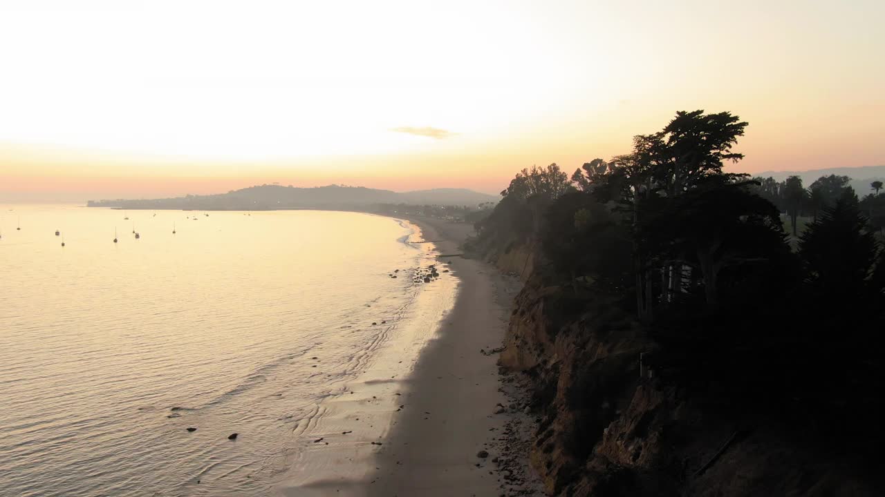 空中拍摄的人在蝴蝶海滩对橙色的天空，无人机飞向前在海滩上溅起的波浪在日落-圣巴巴拉，加利福尼亚视频素材