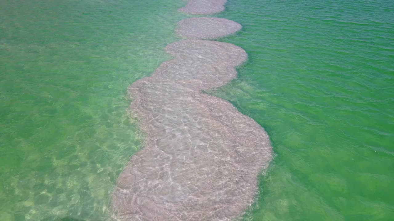 在阳光明媚的一天，无人机在湖上空向前飞行在死海的盐层的航拍视频素材