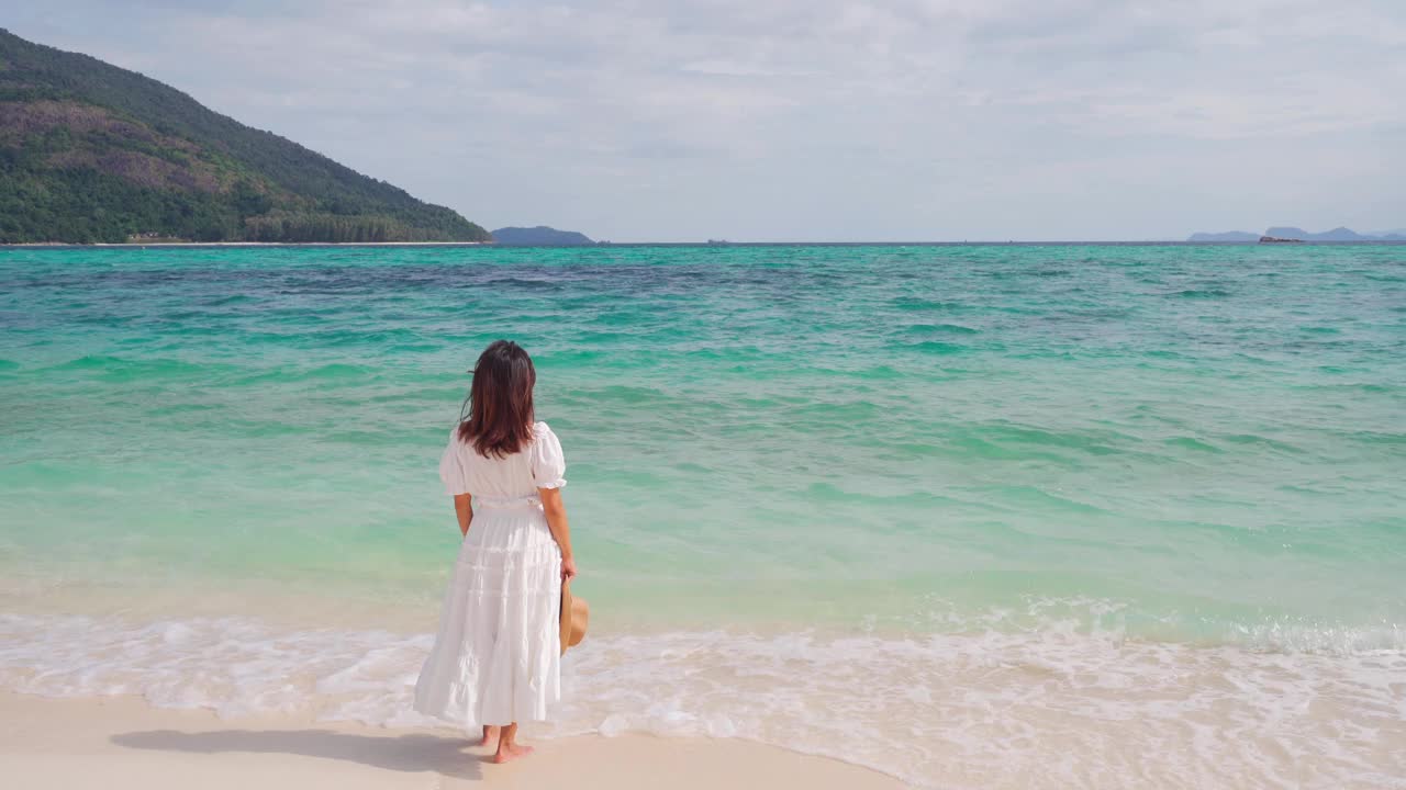 年轻女子旅行者放松和享受美丽的热带白色沙滩与海浪泡沫和透明的海，暑假和旅游概念视频素材