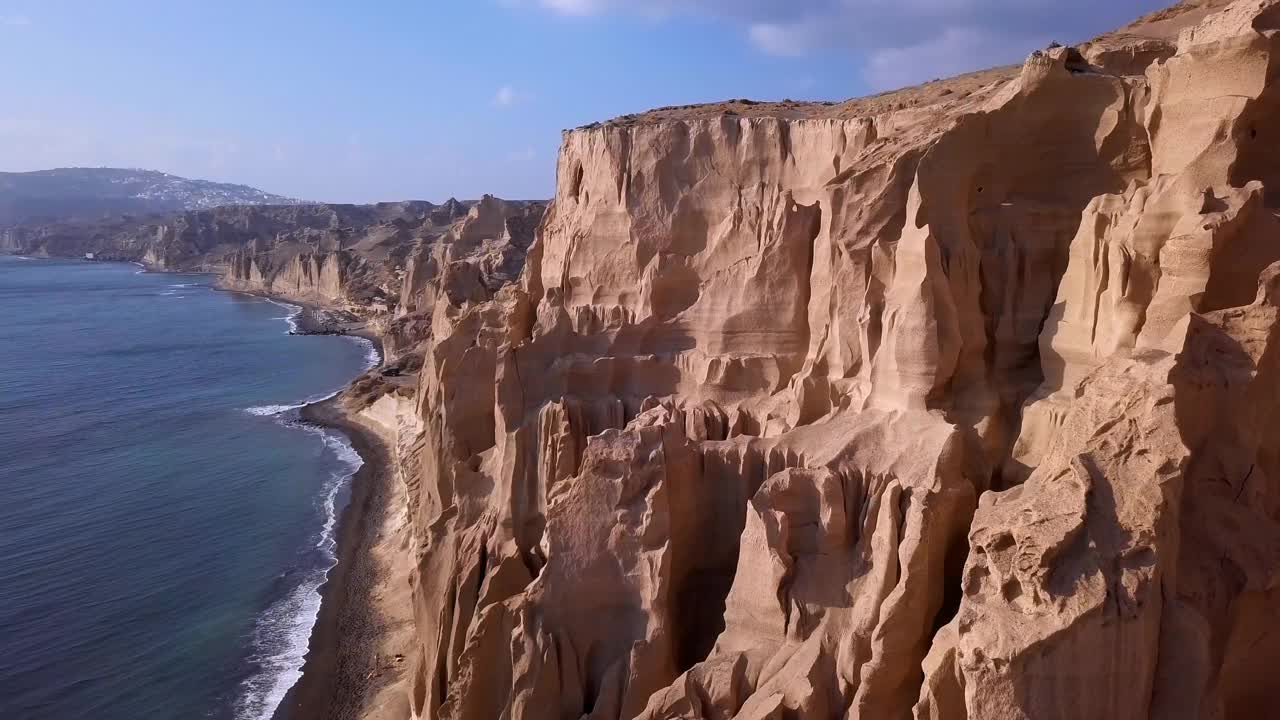 在阳光明媚的日子里，在希腊圣托里尼岛，无人机在海面上飞行，在天空下的帕利亚Vlichada海滩的岩石悬崖拍摄视频素材