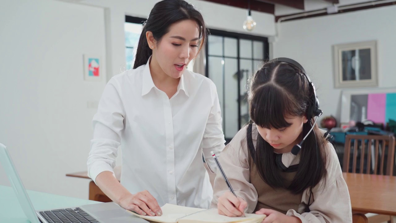 亚洲家庭一起在家学习。小女孩和妈妈在客厅学习教育班。女人和孩子笑和感觉乐趣，享受学习和玩科目在电脑笔记本电脑。视频素材