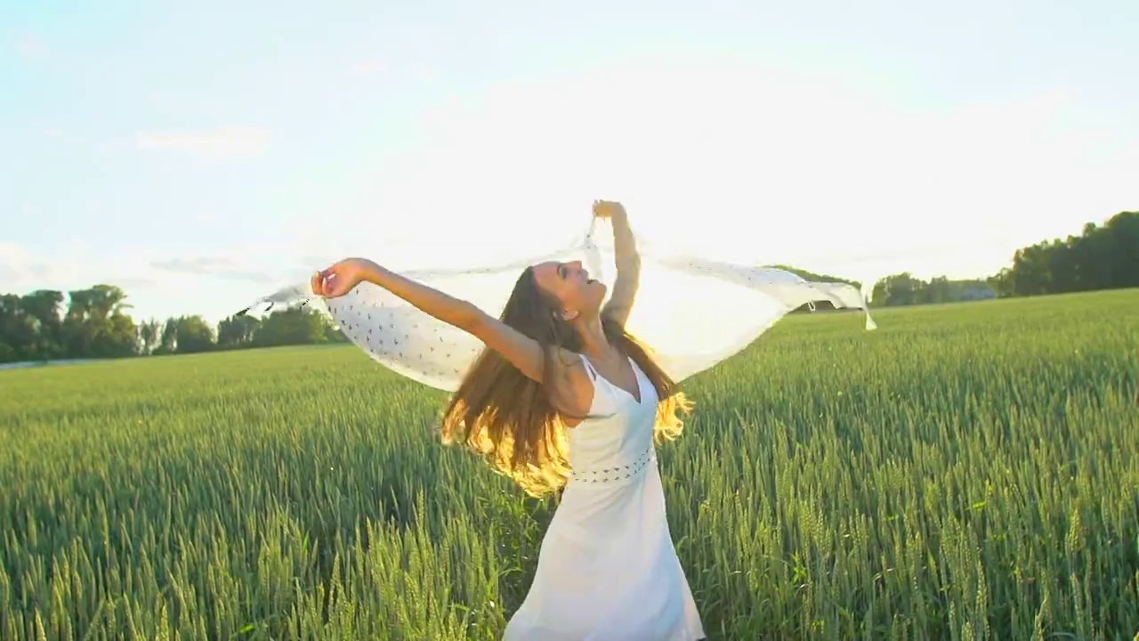 披着围巾的美丽女孩在风中飞舞，在夕阳下的麦田里奔跑视频素材