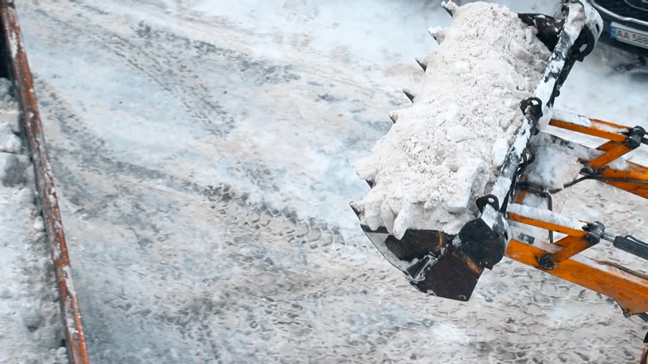 近景上方的拖拉机装载机雪犁铲装载堆雪和冰在自卸车从城市街道在暴风雪降雪清除。视频下载