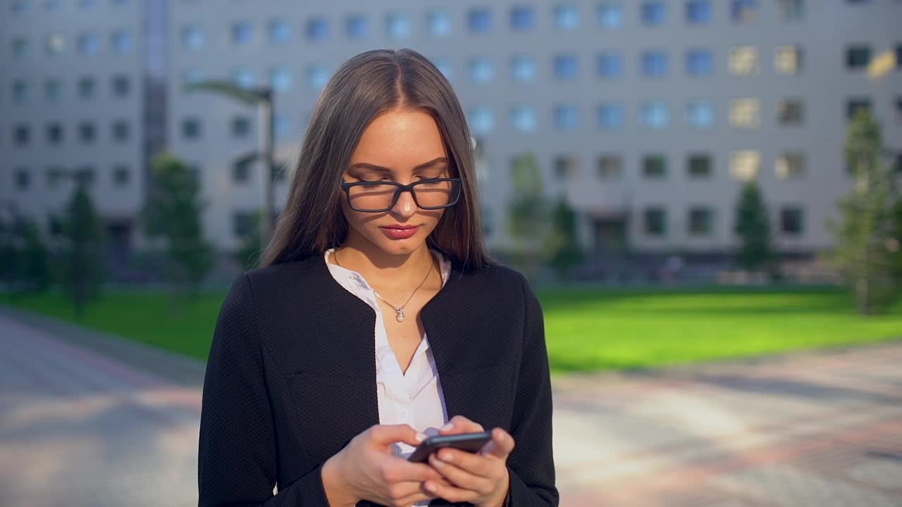 年轻漂亮的女商人或学生穿着白衬衫，在城市里使用现代智能手机视频素材