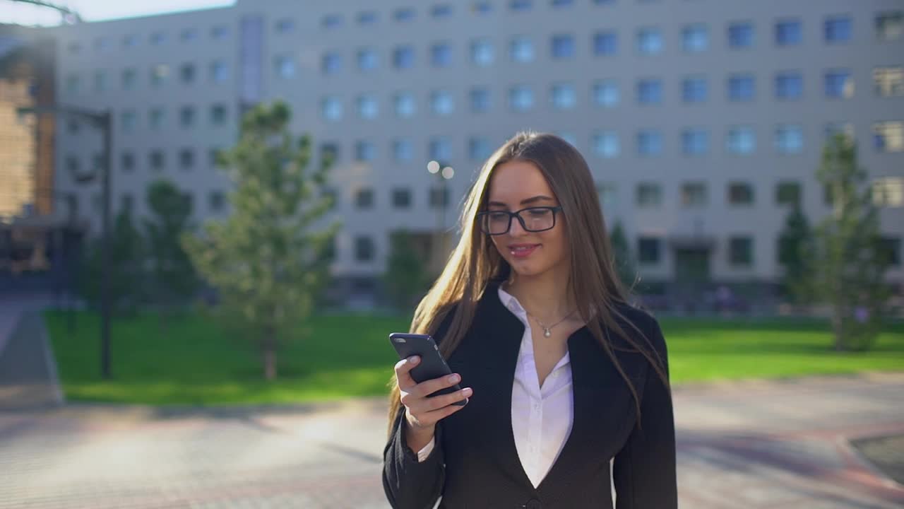 年轻漂亮的女商人或学生穿着白衬衫，在城市里使用现代智能手机视频素材