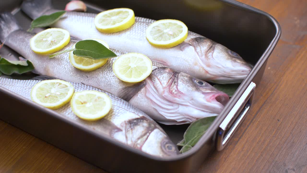 新鲜的海鲈鱼与柠檬片和鼠尾草一起在平底锅中烹煮视频素材