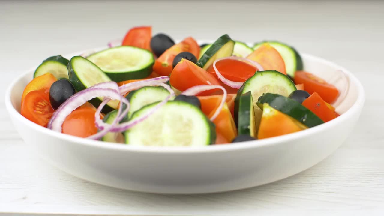 将新鲜的沙拉与红番茄、黄瓜、洋葱和黑橄榄拌上纯橄榄油。慢动作效果视频下载