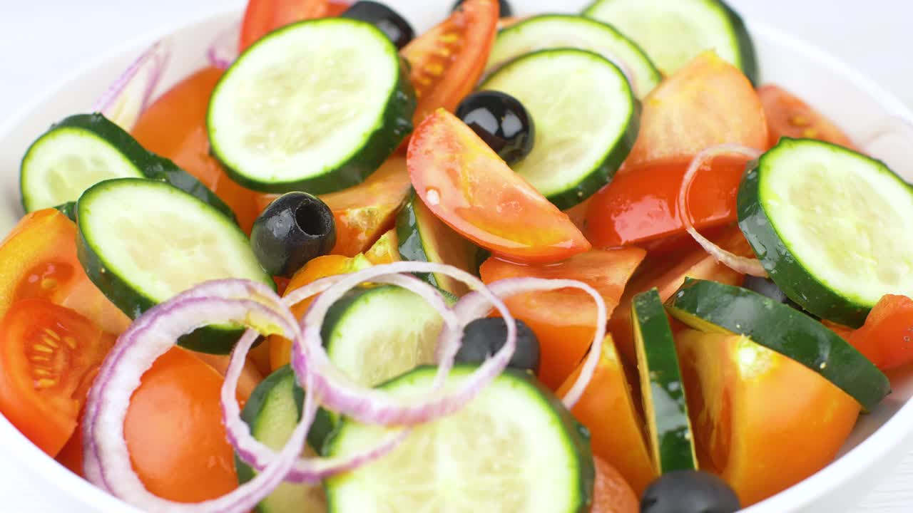 将新鲜的沙拉与红番茄、黄瓜、洋葱和黑橄榄拌上纯橄榄油。慢动作效果视频素材