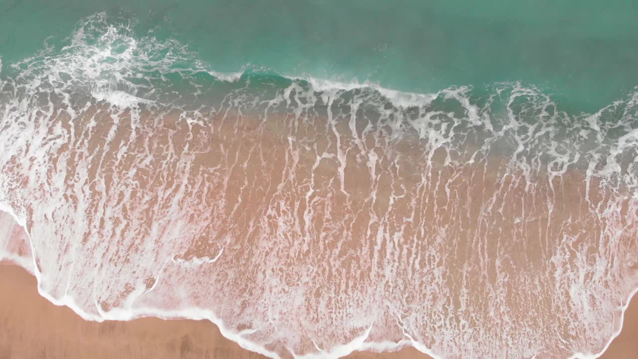 汹涌的蓝色海浪拍打着沙滩。美丽的海浪在暴风雨和白色的泡沫。俯视图的奇妙自然。沙滩和迷人的大海视频素材