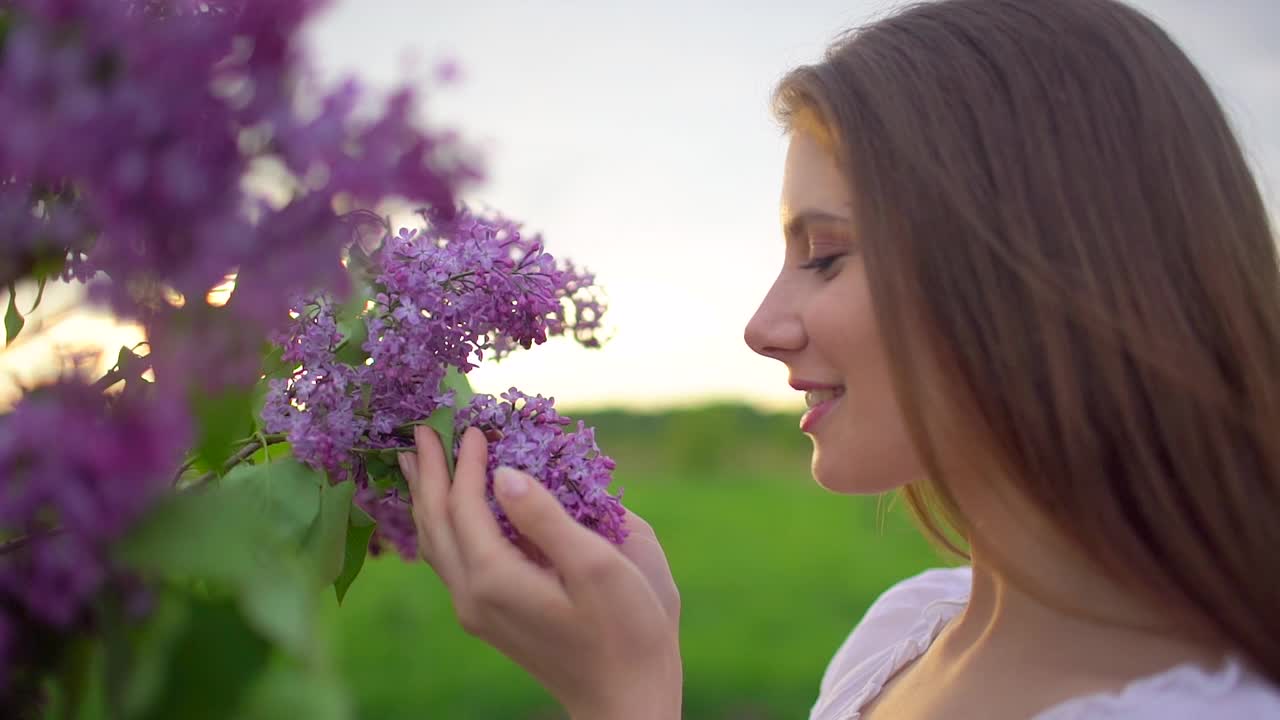 年轻浪漫的微笑美丽的女人女孩嗅闻在大自然的丁香花束视频素材