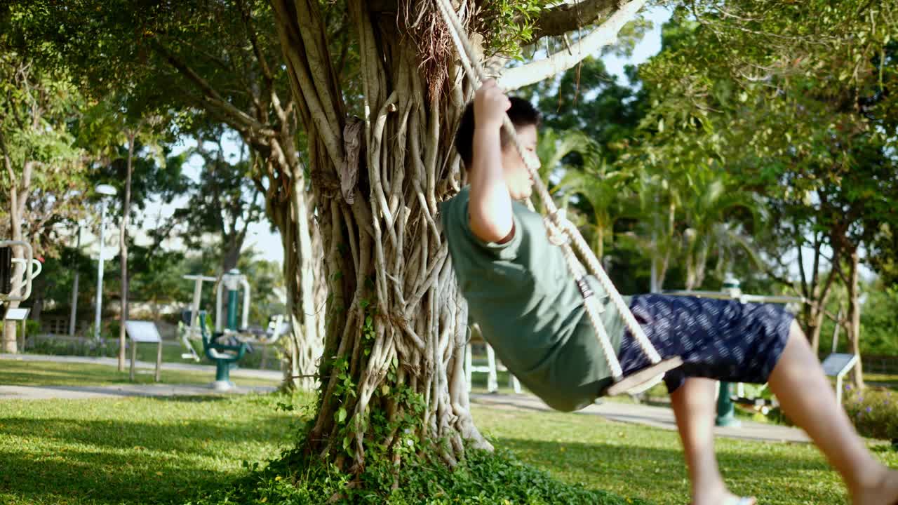 快乐的亚洲十多岁的男孩玩秋千，这是挂在户外公园的树上，生活理念。视频素材