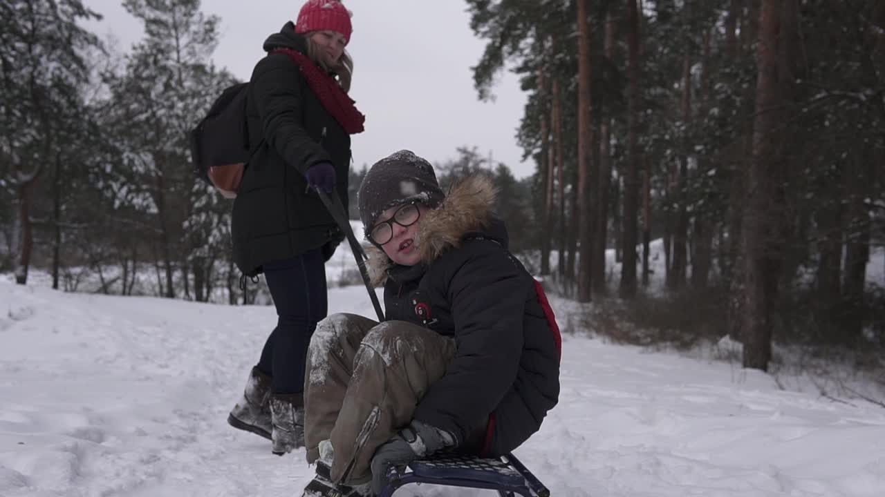 在白雪覆盖的森林里，妈妈带着孩子在雪橇上拉屎。冬季在隔离区的乐趣。视频素材