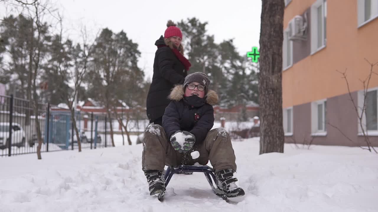 妈妈和孩子在离房子不远的院子里玩雪橇和打雪仗。冬季隔离期间的乐趣。视频素材