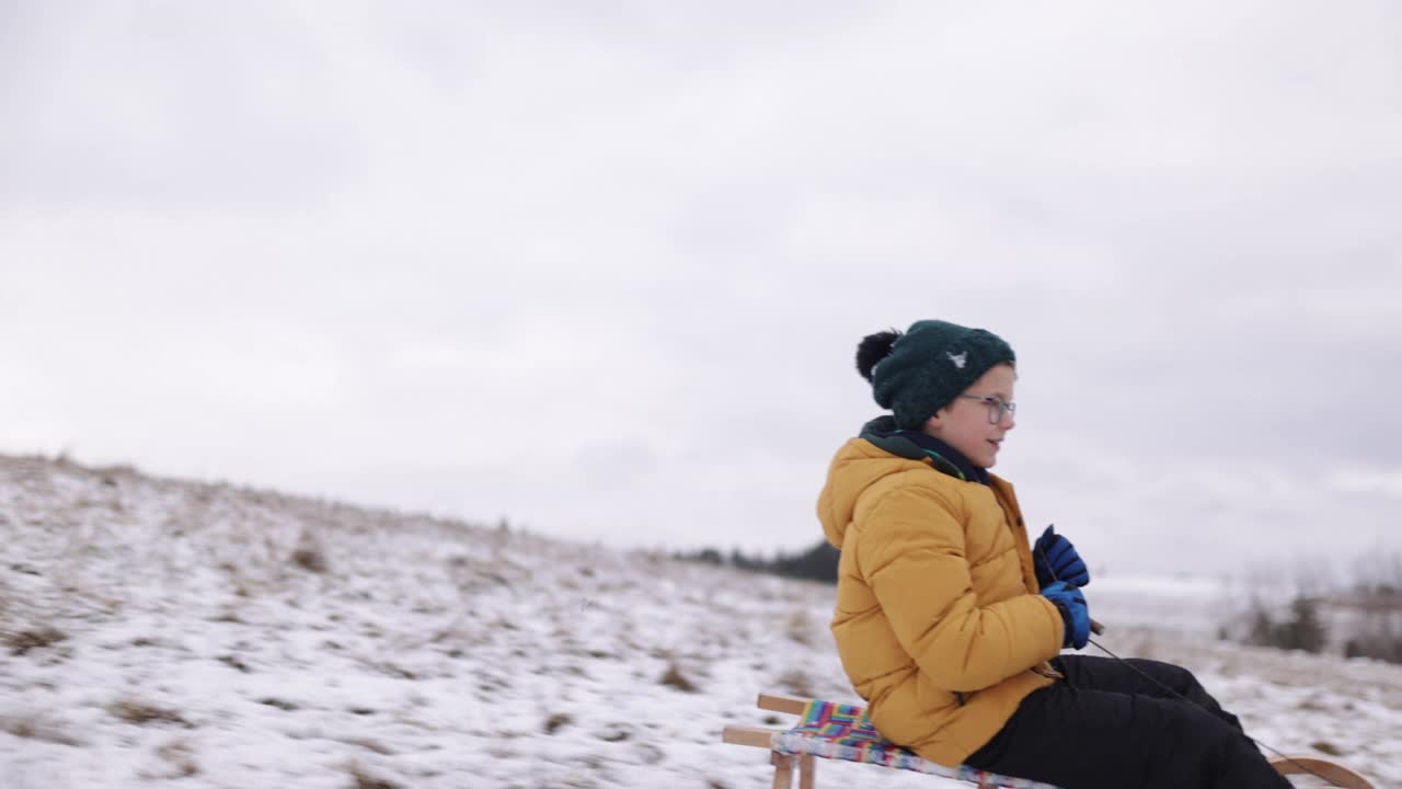 冬天的一天，小男孩在山上拉雪橇视频素材