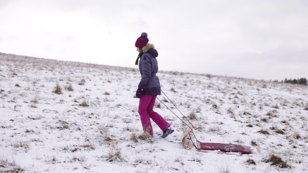 一个十几岁的女孩在冬天的一个小山上拉雪橇视频素材