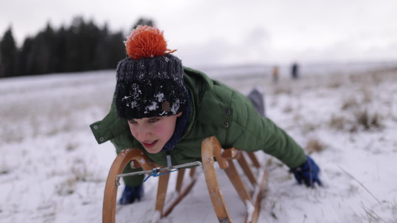 冬天的一天，小男孩在山上拉雪橇视频素材