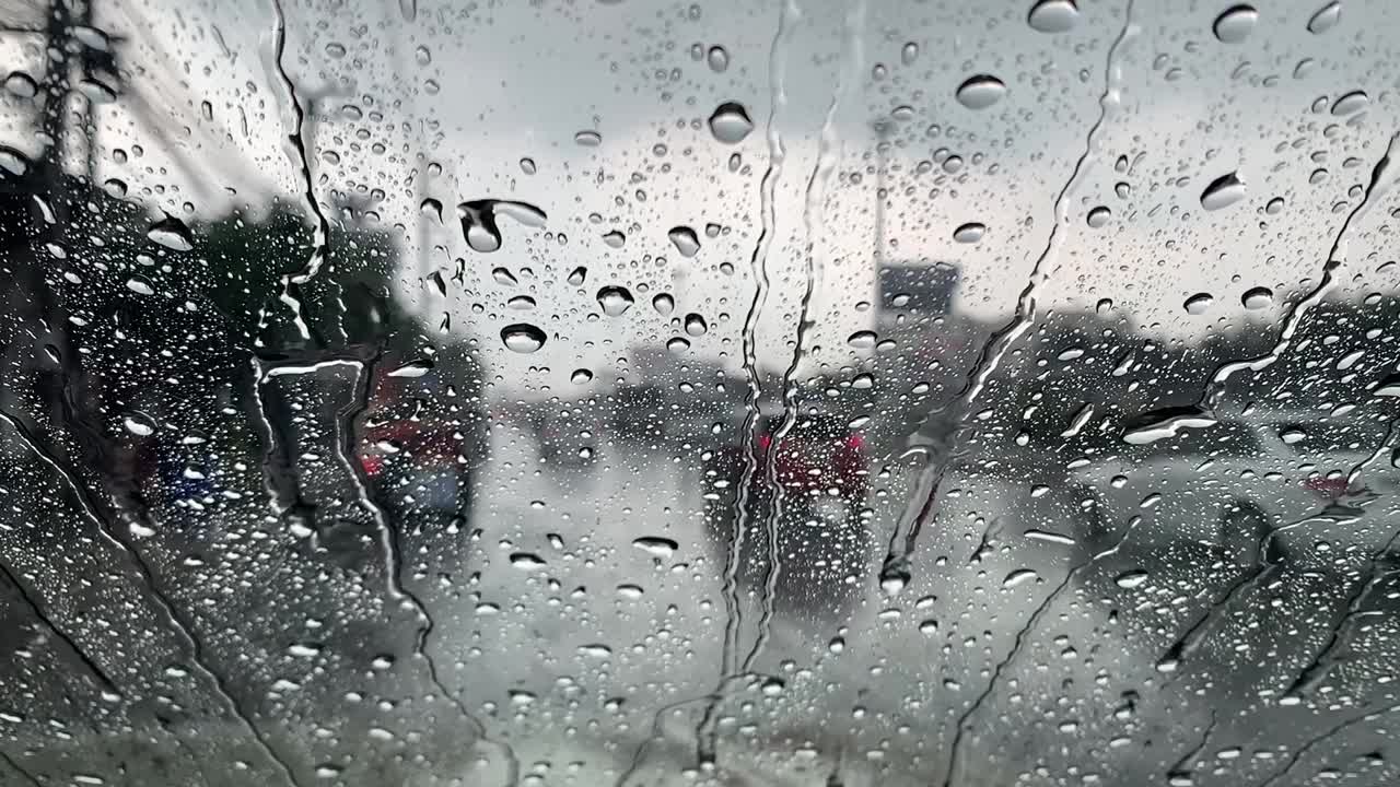 在一个下雨天透过车窗看曼谷的道路交通模糊的景象。雨滴落在汽车的玻璃窗上视频素材