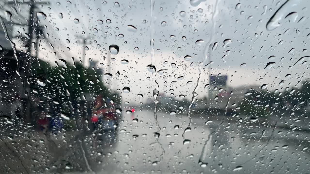 在一个下雨天透过车窗看曼谷的道路交通模糊的景象。雨滴落在汽车的玻璃窗上视频素材