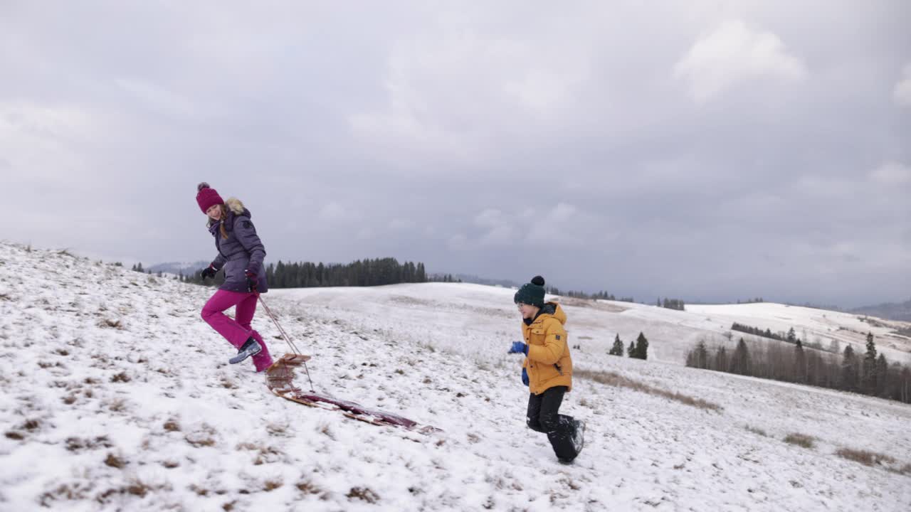 冬天的一天，两个孩子在山上滑雪橇视频素材