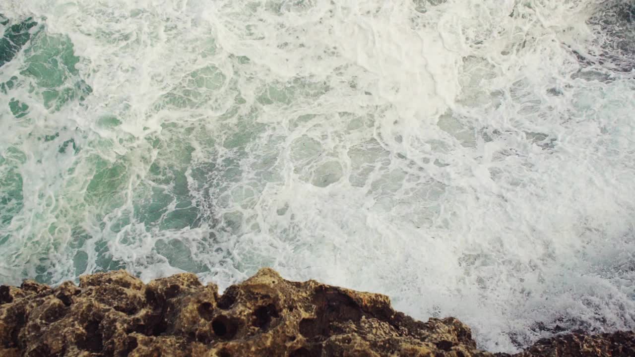 海浪拍打着岩石海岸，绿色的水溅起浪花，产生白色的泡沫，从上面看，慢动作视频视频素材