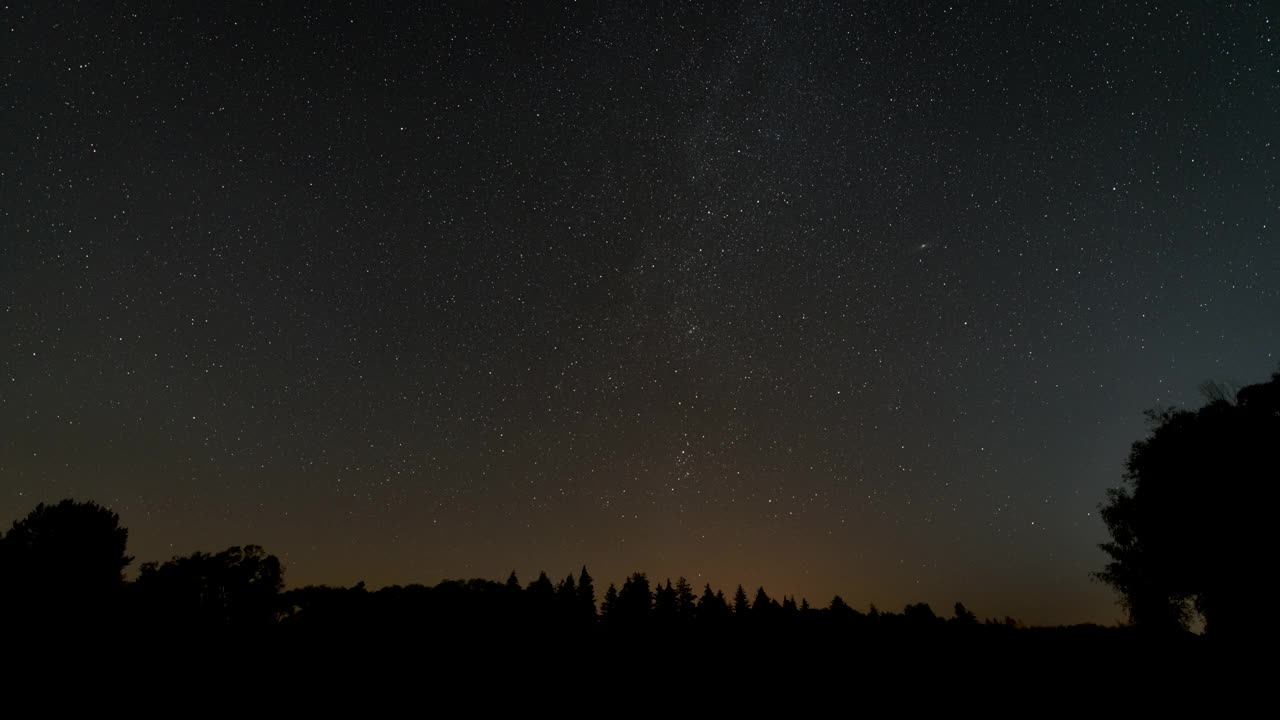 夜晚的时间推移与树的剪影前景-星空一些云经过，银河系和仙女座星系在恒星星座区域隐约可见视频素材