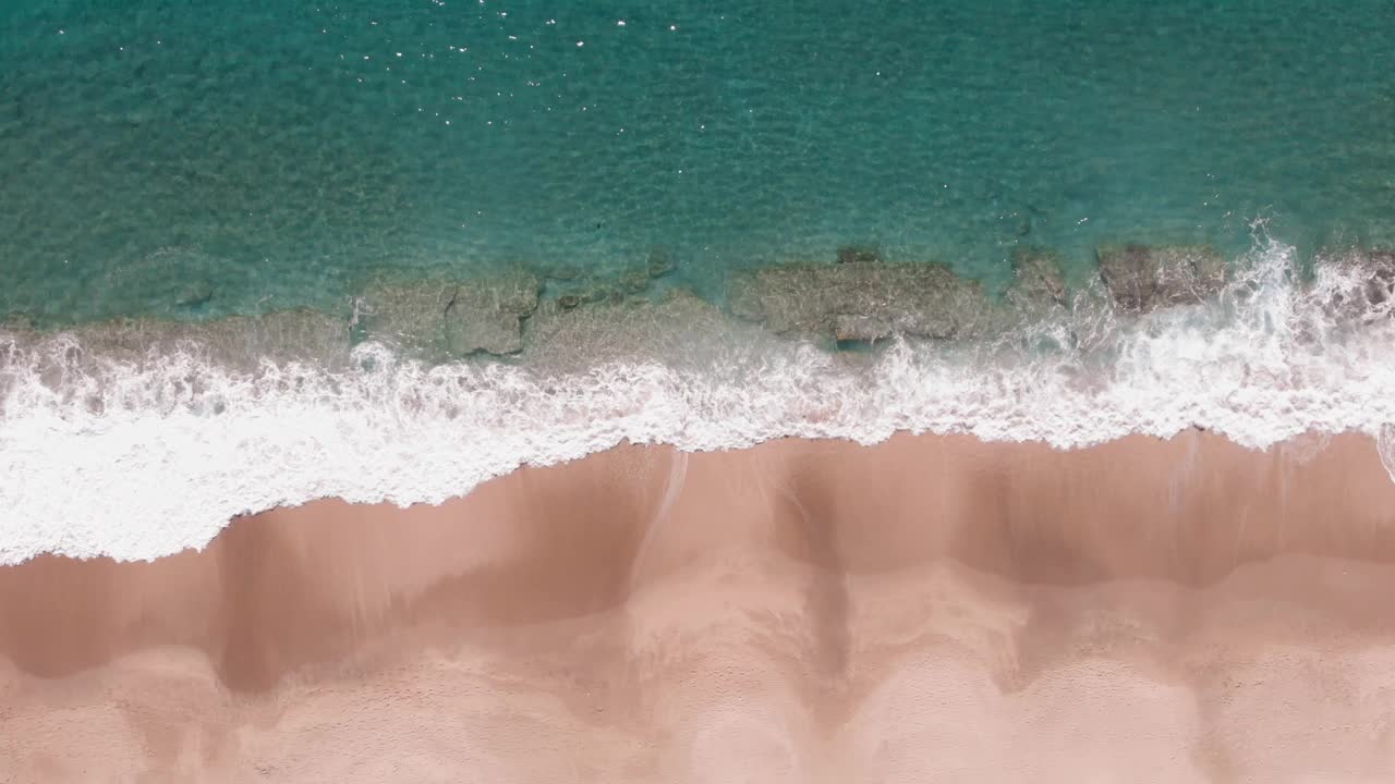 美丽的海景，金色的沙滩和绿松石般的清澈海水。海浪拍打着沙滩，溅起水花。夏季热带海滩的无人机视图。空旷而干净的海岸视频素材