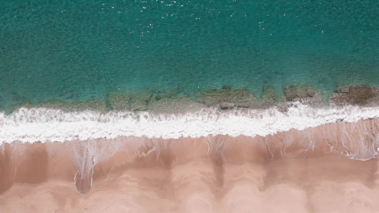 海滩上海浪的鸟瞰图。海浪在沙滩上翻滚，撞击和溅起水花。美丽的海浪拍打着海岸。美丽的海景视频素材