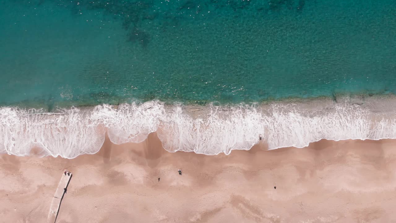 从空中俯瞰，海浪撞击着金色的海滩。清澈的绿松石大海和波浪。有海浪和白色泡沫的沙滩。美丽的沙滩顶视图视频素材