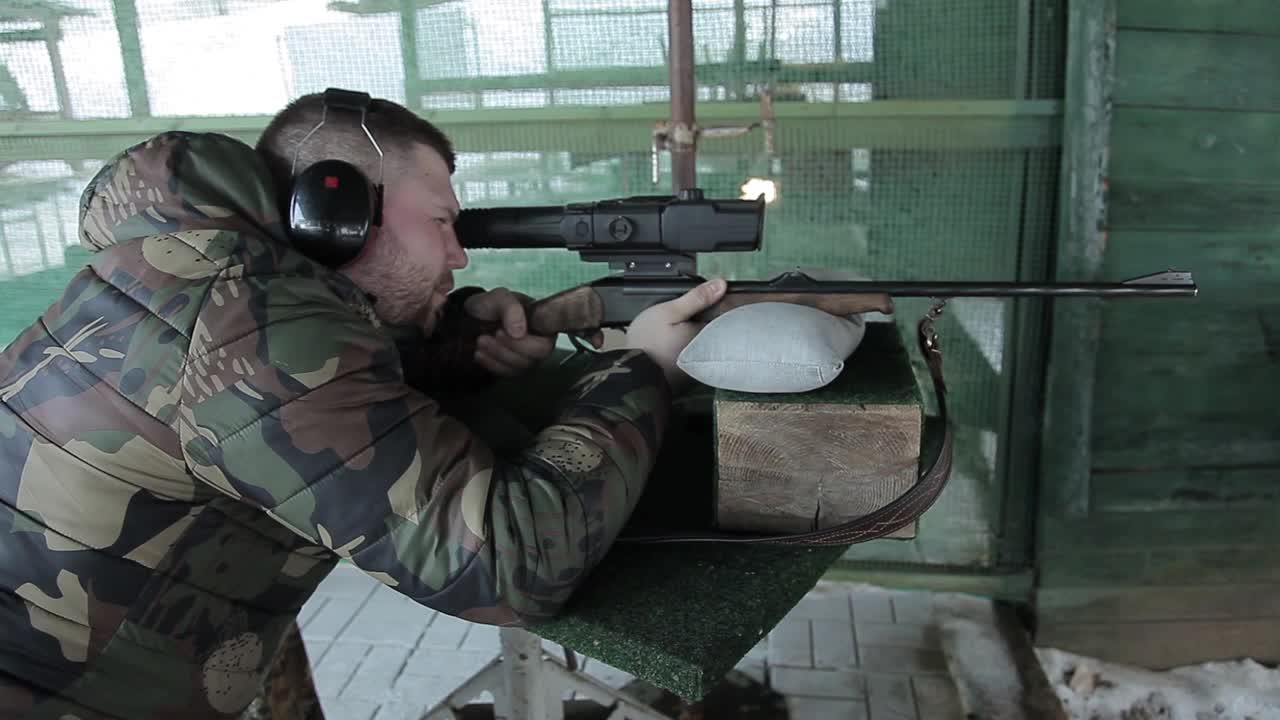 男性射手猎人通过视线瞄准。在射击场网球场进行射击训练。一名穿着迷彩服、戴着耳机的男子准备向目标射击。视频素材