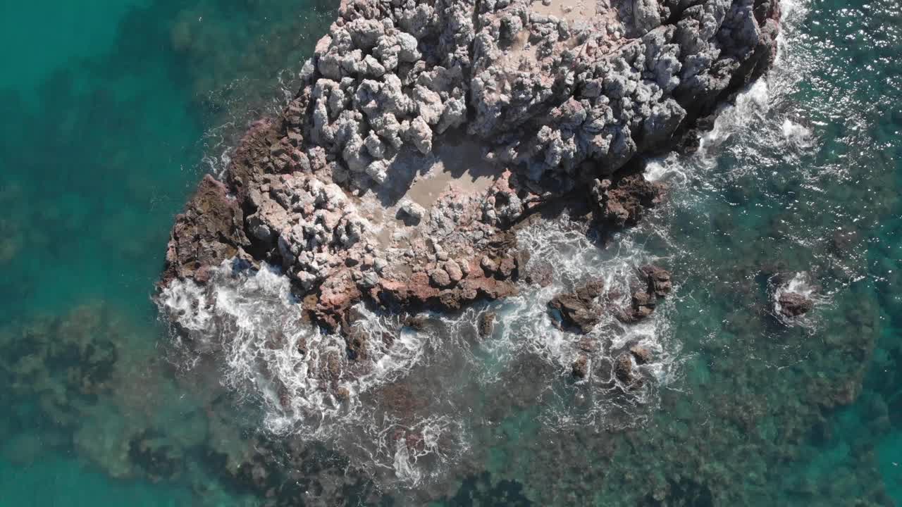 在蓝色的海洋里，海浪拍打着岩石，溅起白色的泡沫。美丽的海浪冲击着岩石。鸟瞰图的海浪打破了空的石头岩石悬崖视频素材