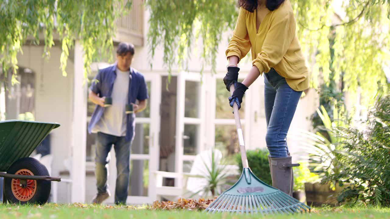 成熟的亚洲妇女耙和整理在花园的叶子，丈夫给她的热饮料在杯子-镜头的慢动作视频素材