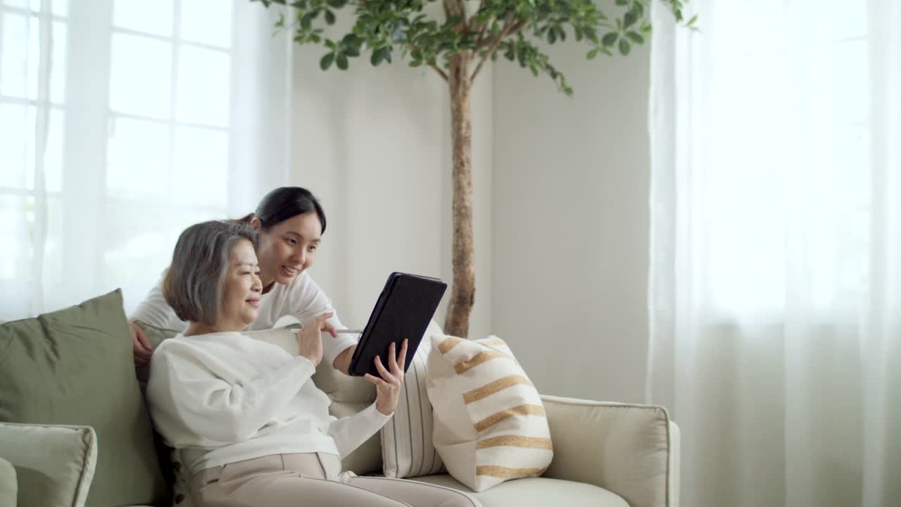 年轻女子和她的母亲一起在家里使用数码平板电脑视频素材