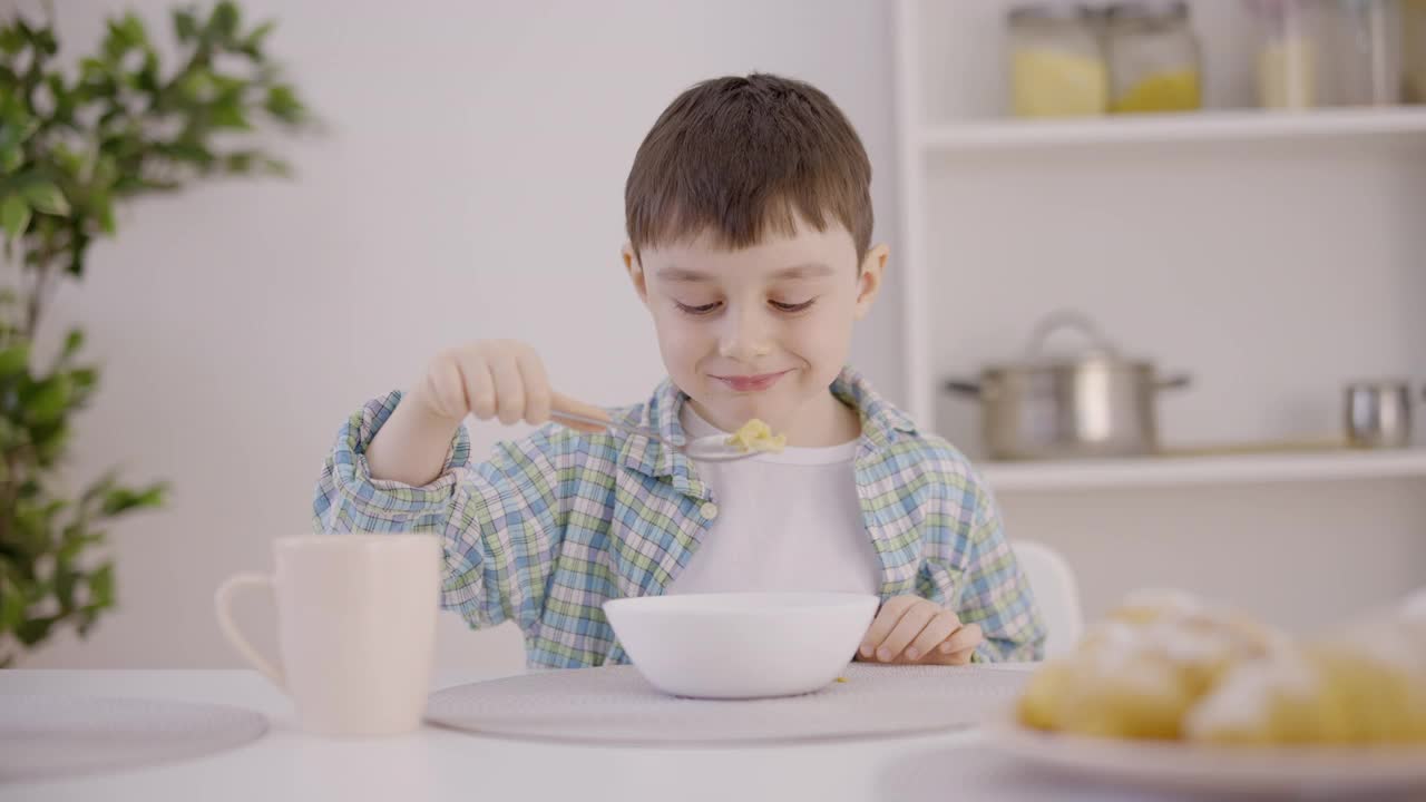 快乐的小男孩坐在厨房的餐桌上吃午饭，健康营养视频素材