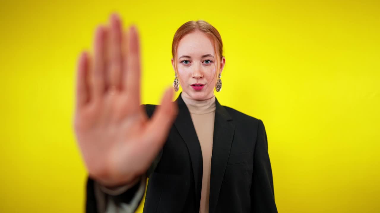 女性手的特写与模糊红发女人在黄色的背景。年轻苗条的白人女士显示停止手势。拒绝与拒绝概念视频素材