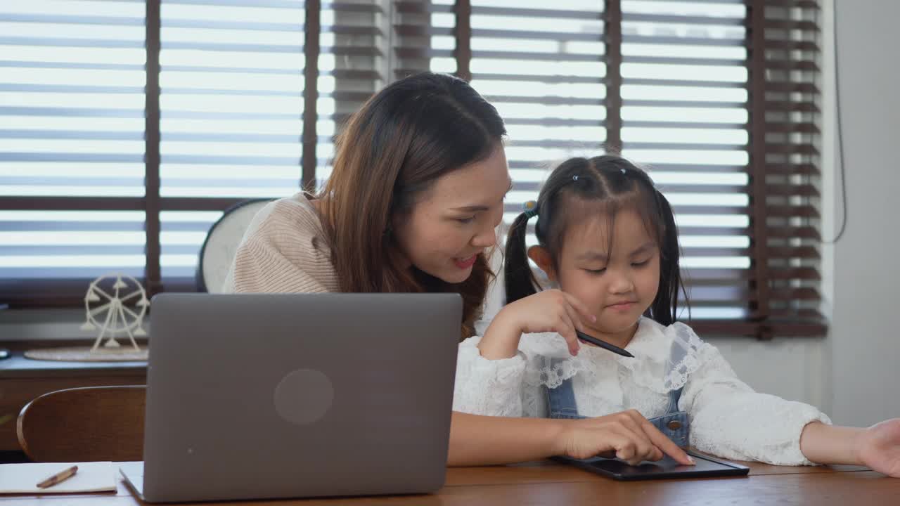 妈妈在家里用笔记本电脑工作，帮助女儿做作业视频素材