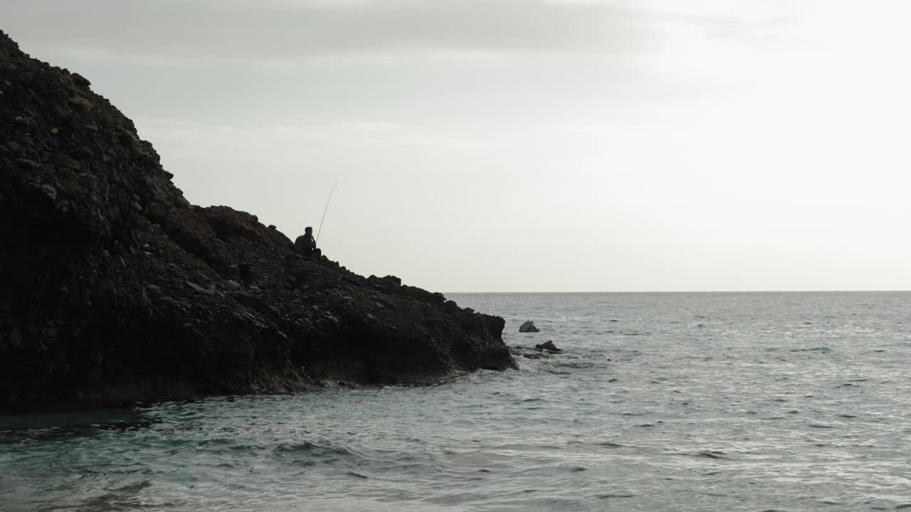 渔夫在海边悬崖边捕鱼的剪影。海浪拍打着岩石峭壁，溅起水花视频素材