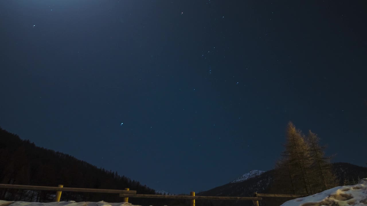 时间流逝:猎户座在月光下的夜空中跳舞，越过雪山和高山落叶松森林。视频素材