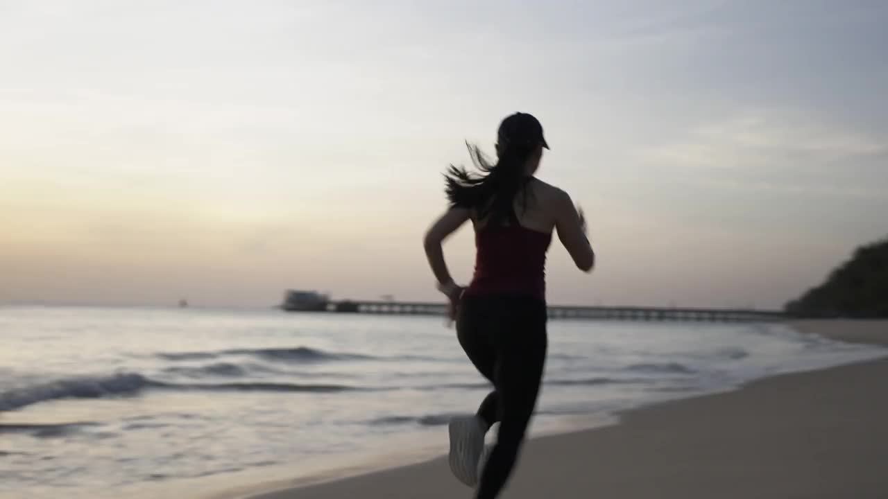 运动女子慢跑，在沙滩上跑步。视频素材