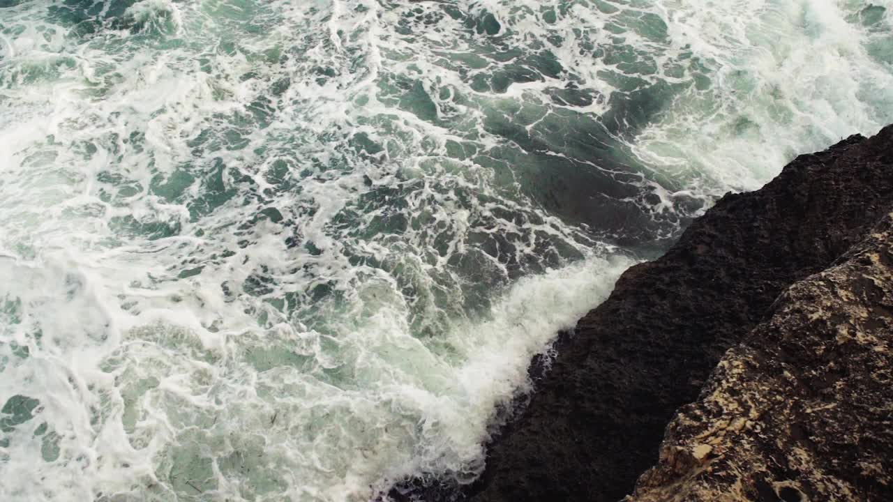 海浪拍打着岩石海岸，绿色的水溅起浪花，产生白色的泡沫，从上面看，慢动作视频视频素材