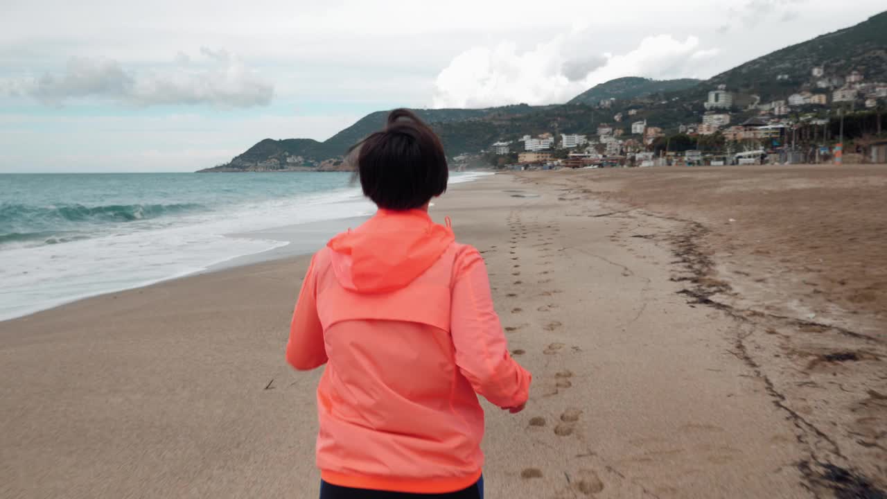 后面跟随的年轻女子是在海滩上跑步在早上。有运动动机的女性在海边慢跑。女游客沿着风景如画的热带海滩慢跑。健身运动的概念视频素材