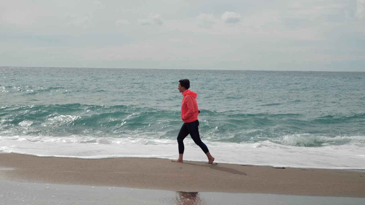 孤独的雌性沿着巨大的海浪走在沙滩上。女人在风雨交加的日子里欣赏海景。海洋风暴。女游客走在海边视频素材