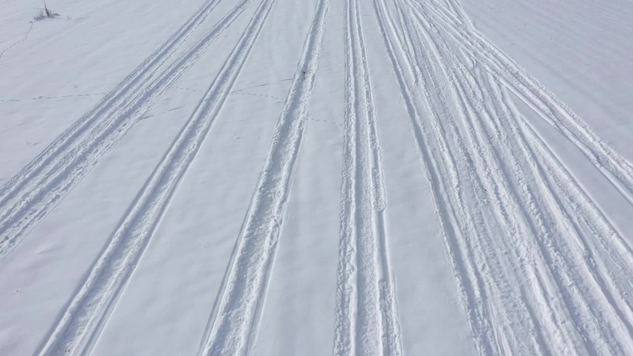 在4K雪天航拍视频中，在车辆轮胎痕迹上方缓慢飞行视频素材