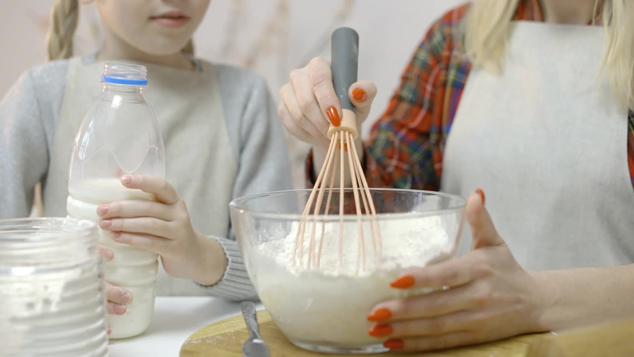 小女儿帮妈妈做饭，把牛奶和面粉倒在碗里，特写视频素材