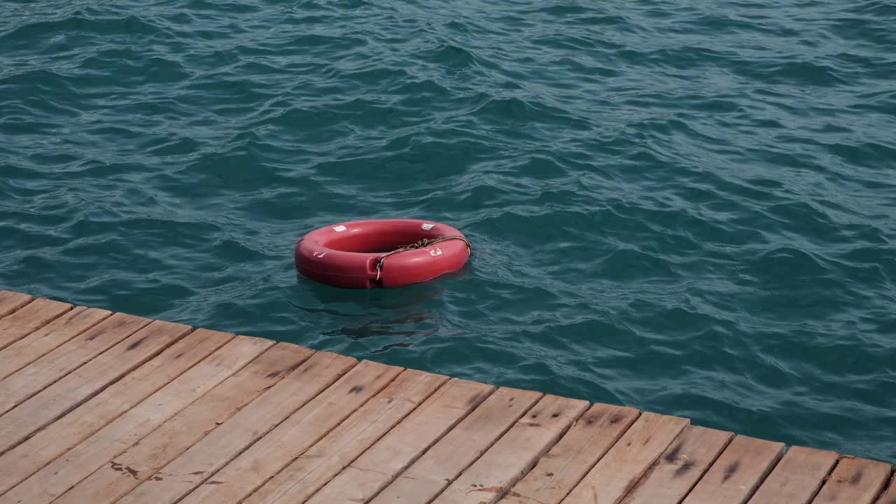 红色救生圈或安全环漂浮在码头附近的蓝色海水中。视频素材