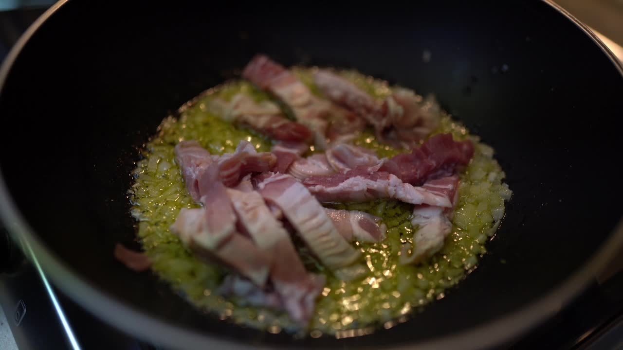 意大利干酪意面的制作过程，用嘶嘶作响的橄榄油在平底锅里炸白洋葱和培根片。不健康饮食的概念视频素材