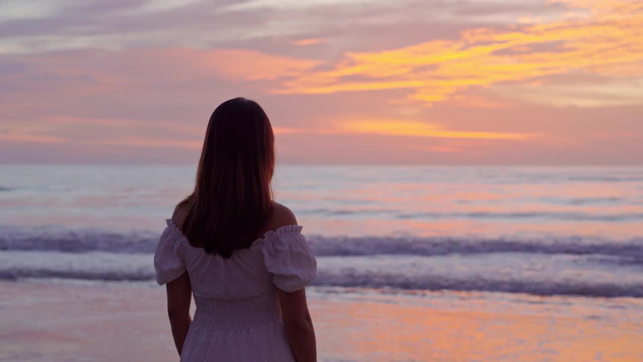 一个孤独的年轻亚洲女人站在沙滩上看着夕阳视频素材